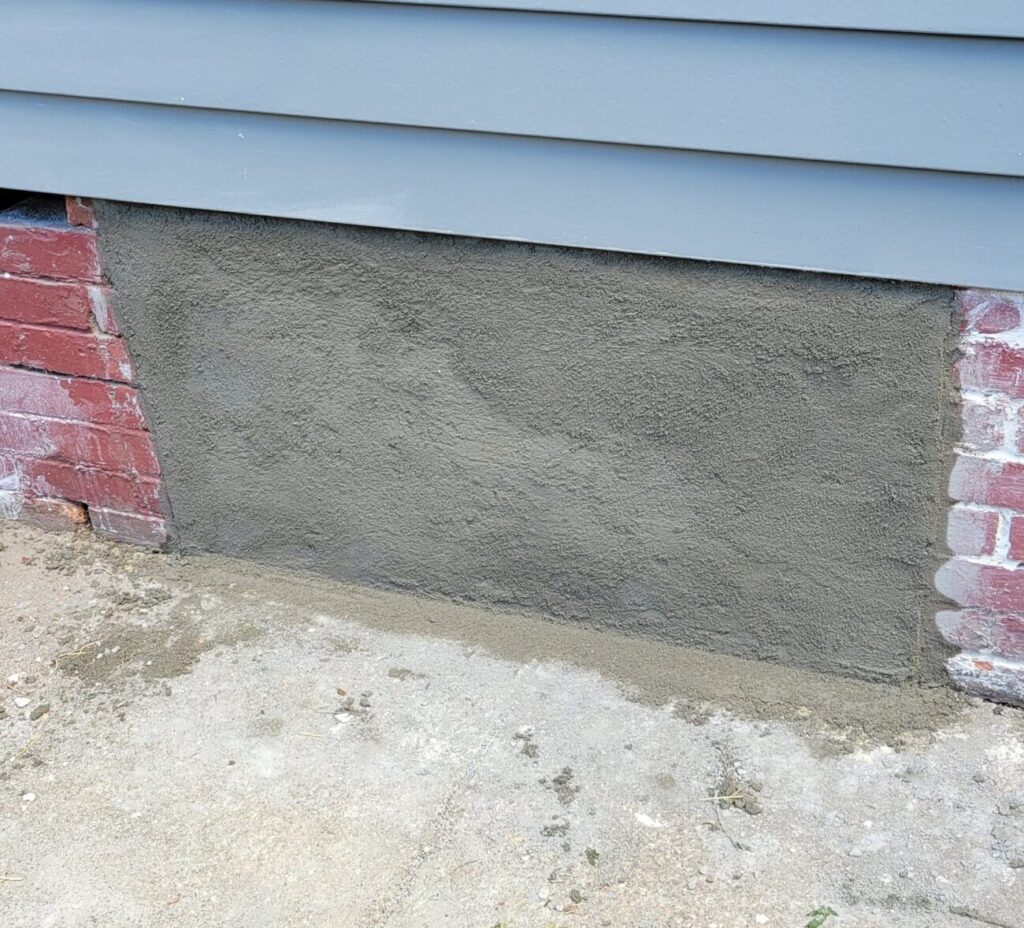 a small concrete patch on the brick foundation of a house